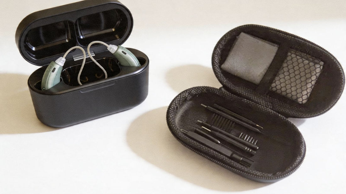 A close-up photograph of a pair hearing aids resting on a clean white surface beside an 8 piece hearing aid cleaning kit